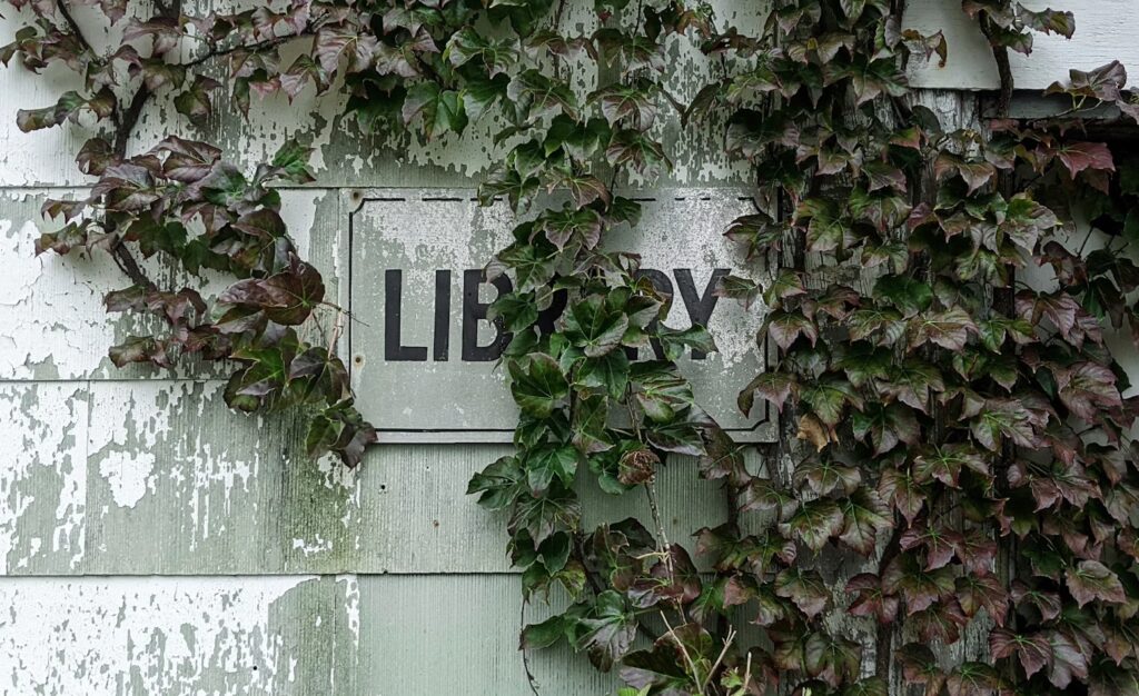 Ein Schild mit "Library" ist von Efeu bewachsen. 